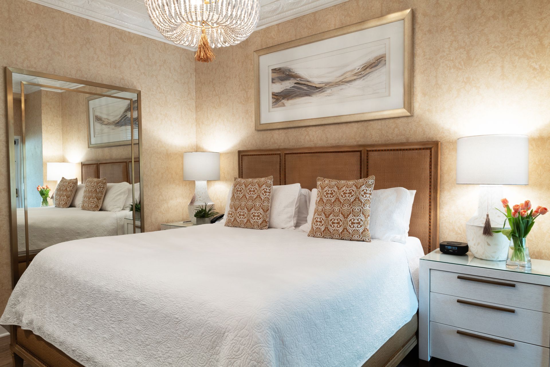 A hotel room with a king size bed , nightstand , mirror and chandelier.