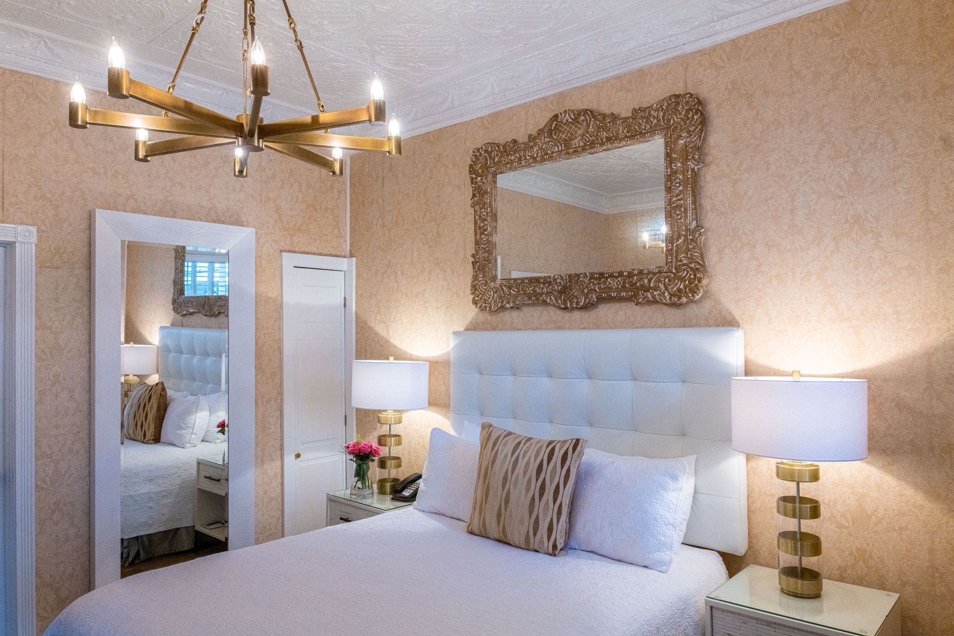 A bedroom with a bed , lamps , a mirror and a chandelier.