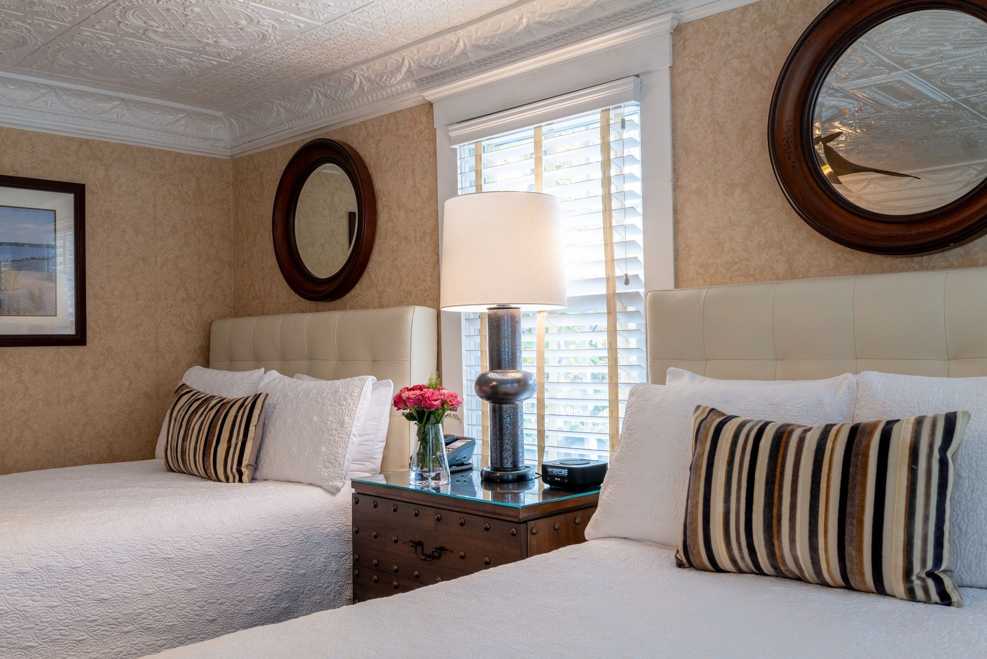 A hotel room with two beds , a nightstand , a lamp and two mirrors.