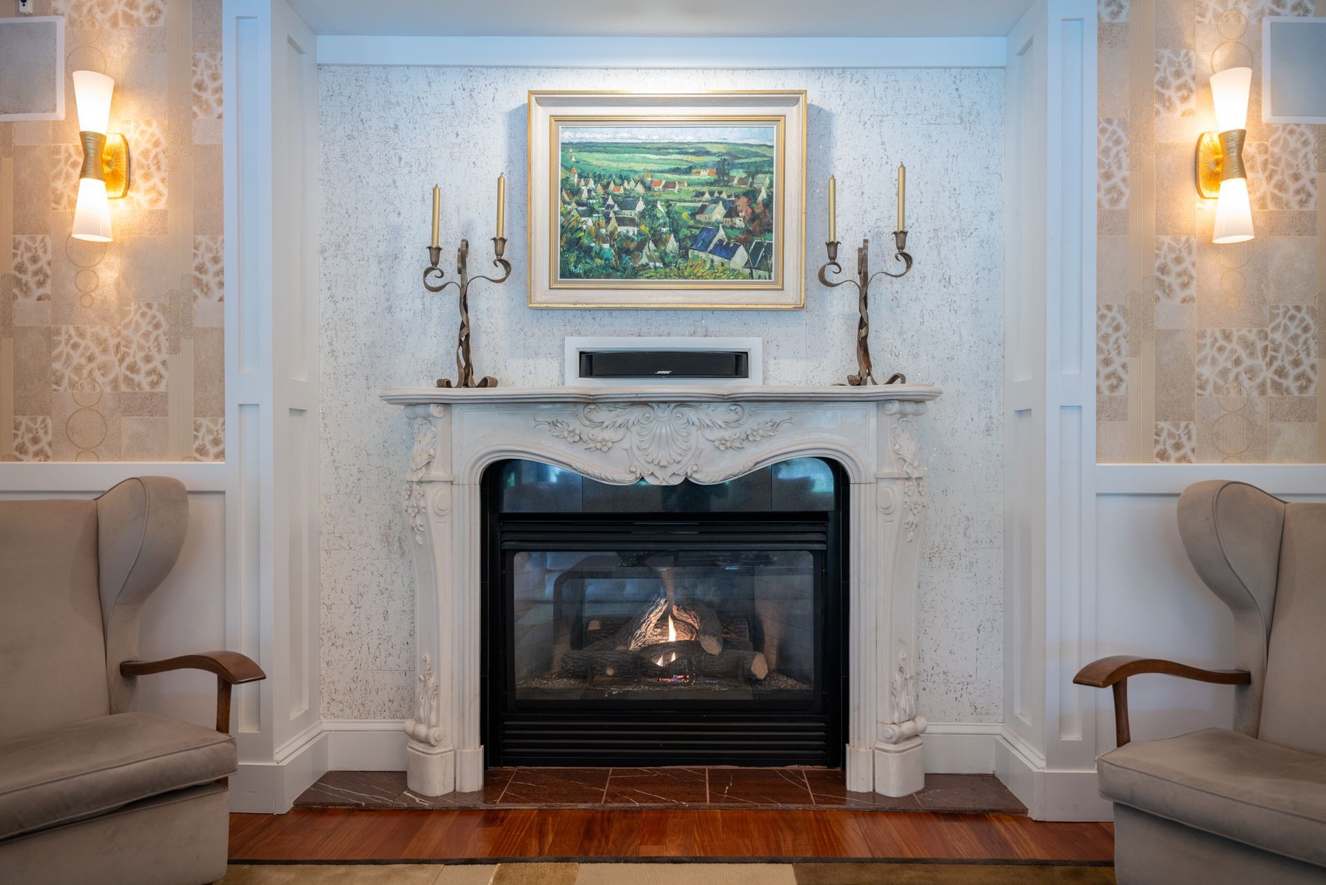 A living room with a fireplace , chairs and a painting on the wall.