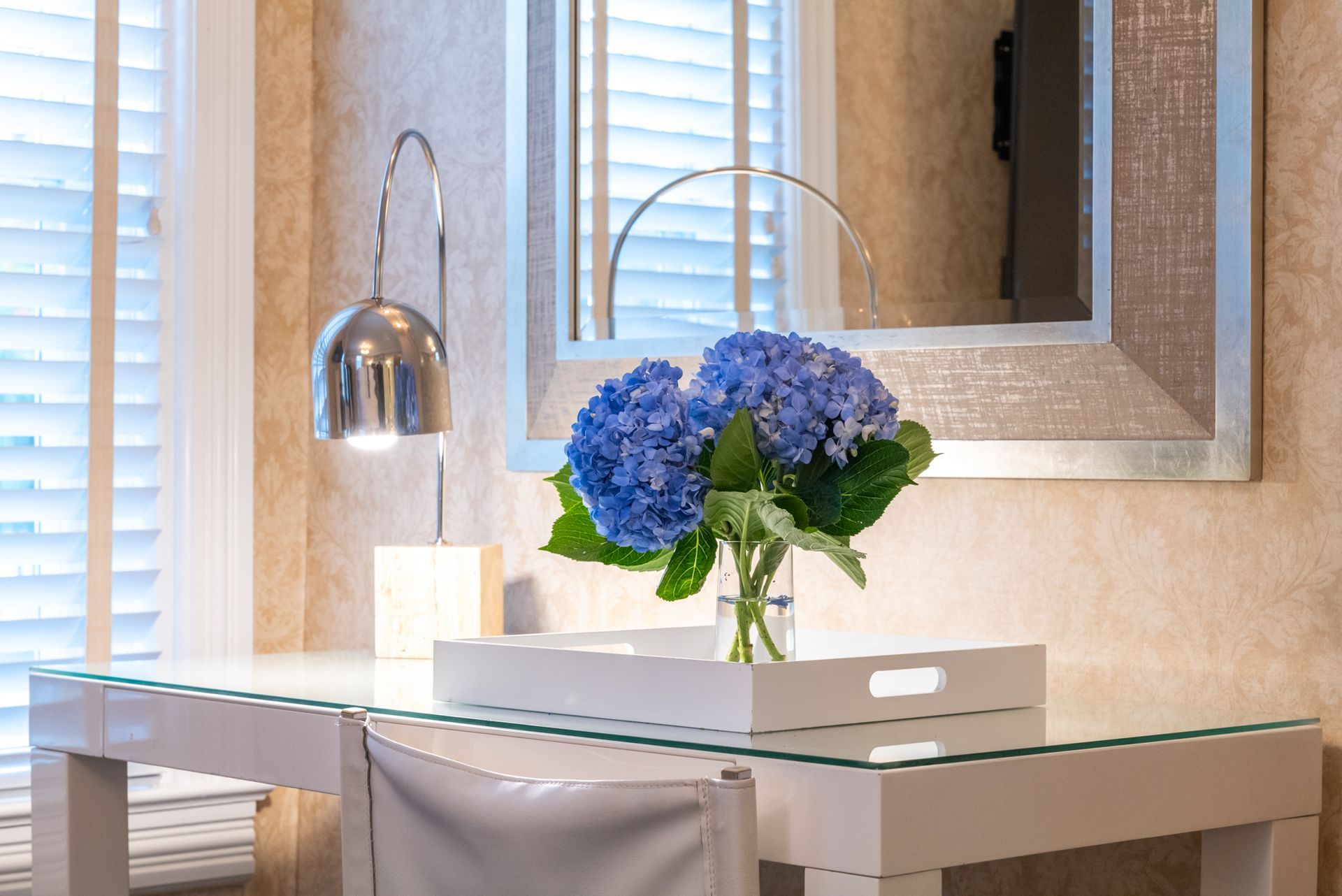 A vase of blue flowers is sitting on a glass table next to a mirror.