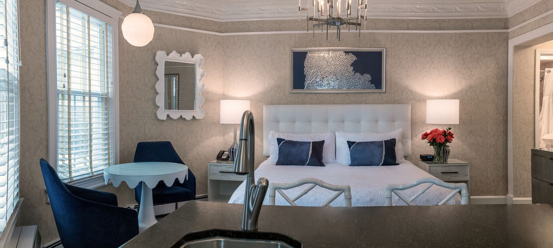 A hotel room with a bed , chairs , table and sink.