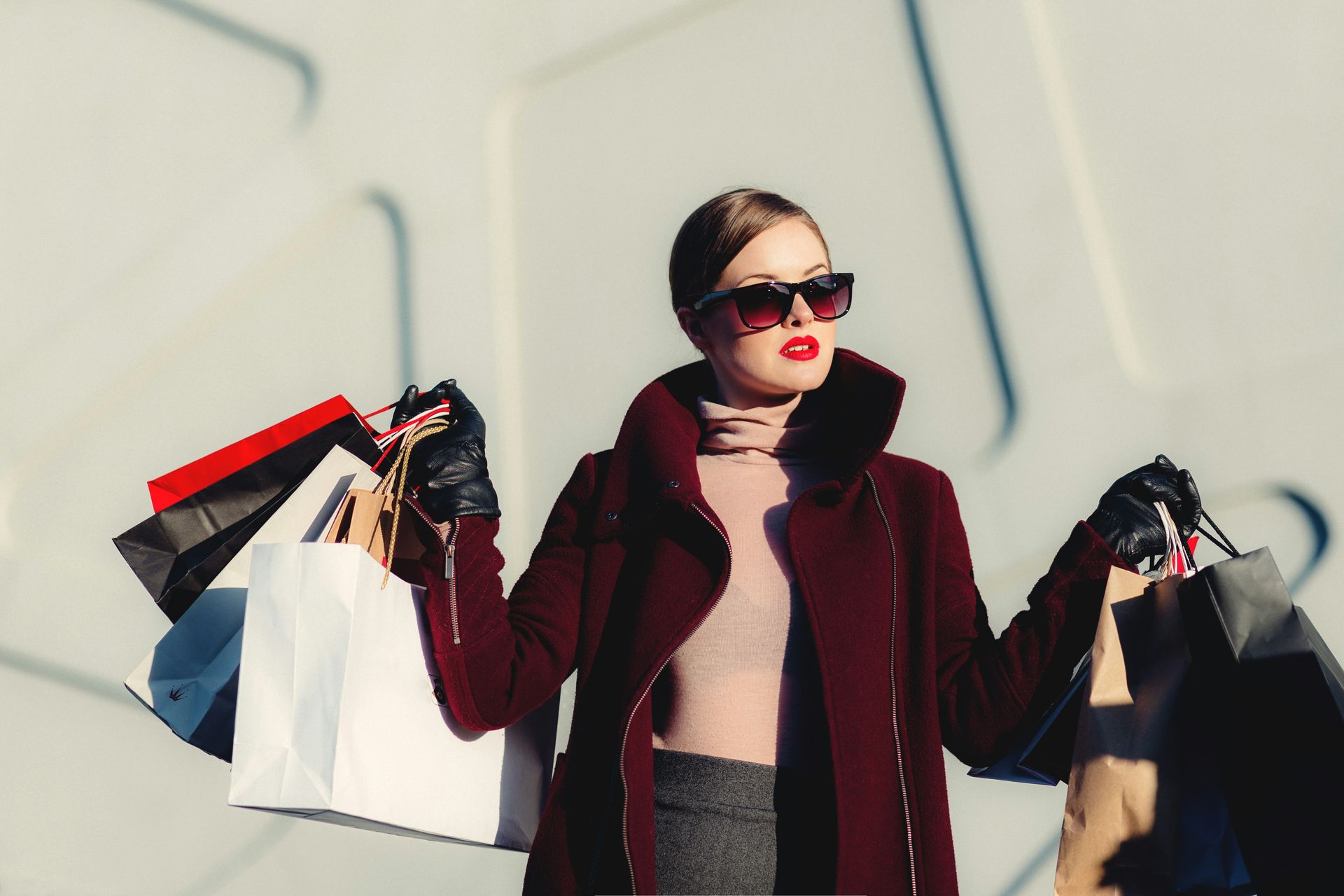 A woman in a red coat is holding a bunch of shopping bags.