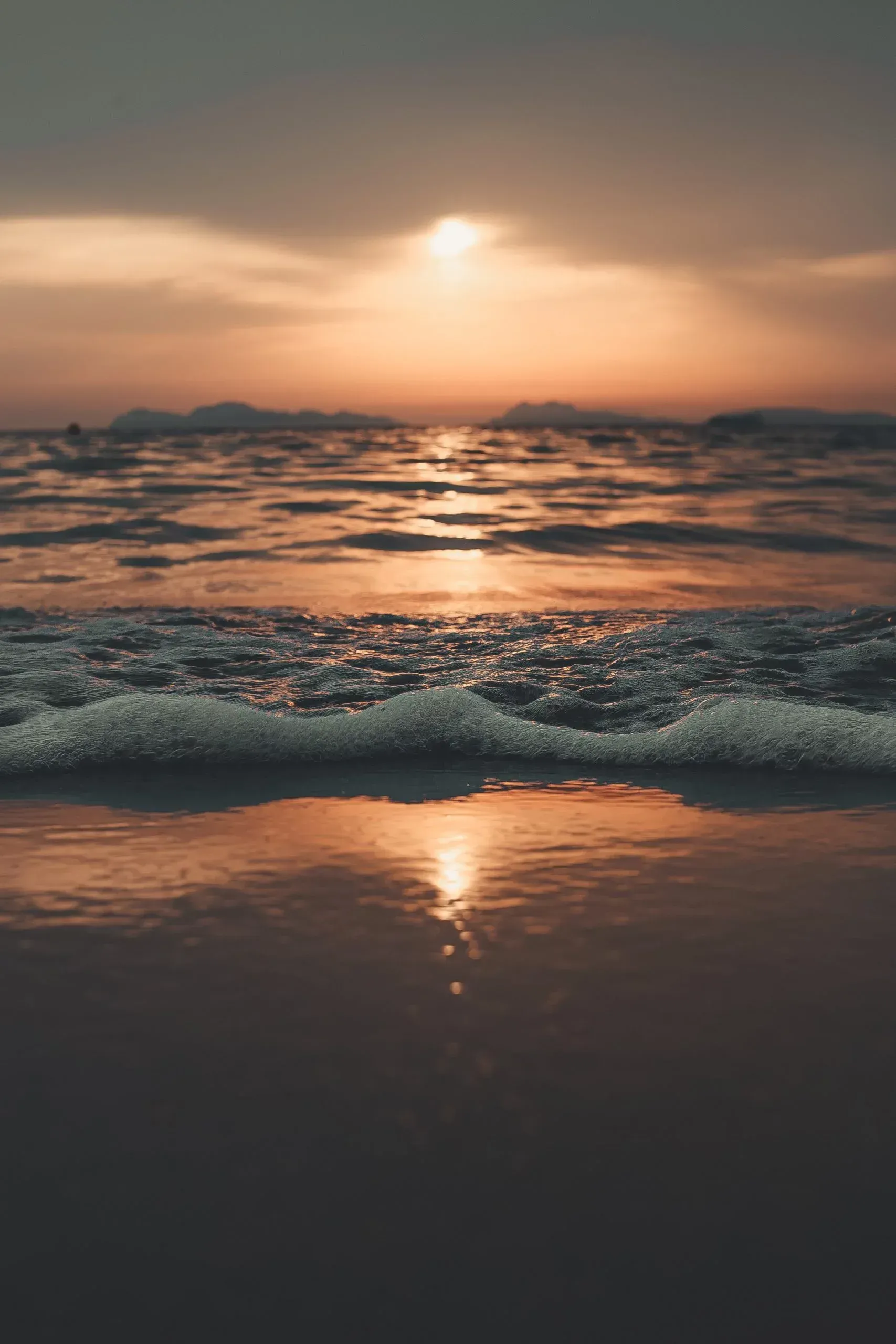 The sun is setting over the ocean and the waves are crashing on the beach.