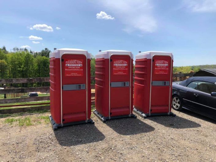 Three red portable toilets are lined up in a parking lot next to a car.