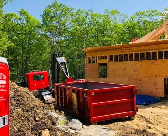 A red portable toilet is sitting in front of a wooden fence.