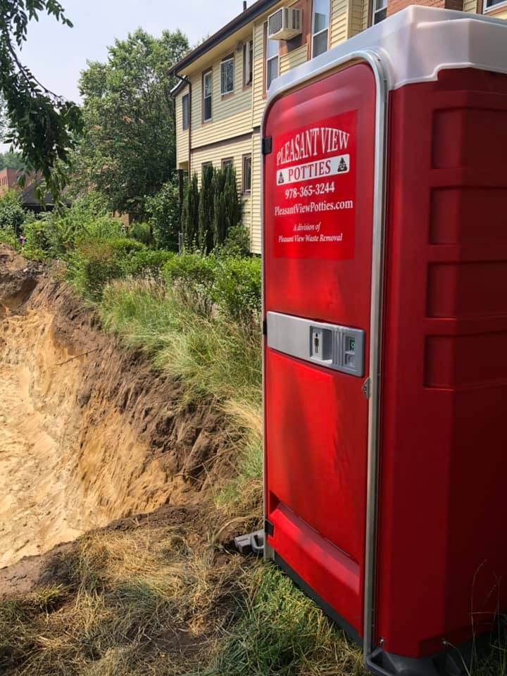 A red portable toilet is parked in front of a house.