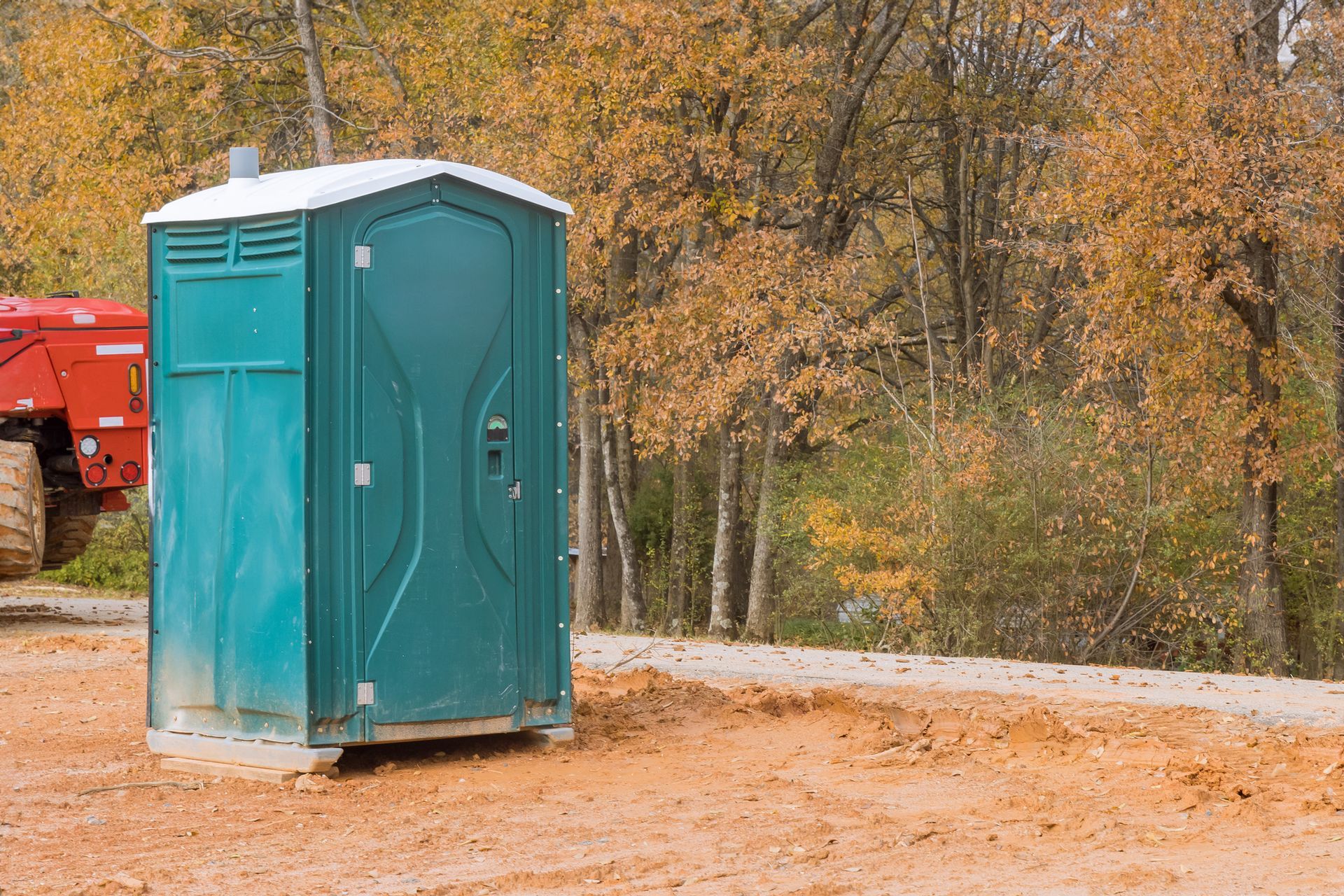 A green portable toilet is sitting in the middle of a dirt road.