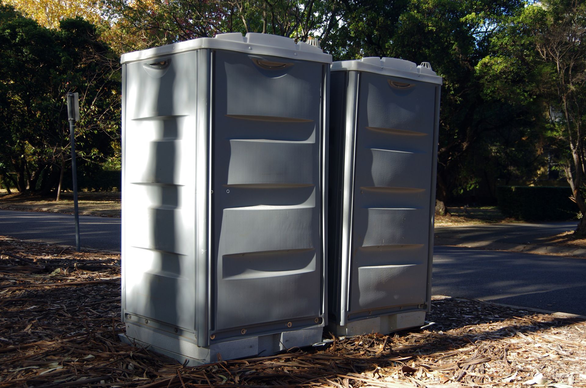 Two portable toilets are sitting next to each other in a park