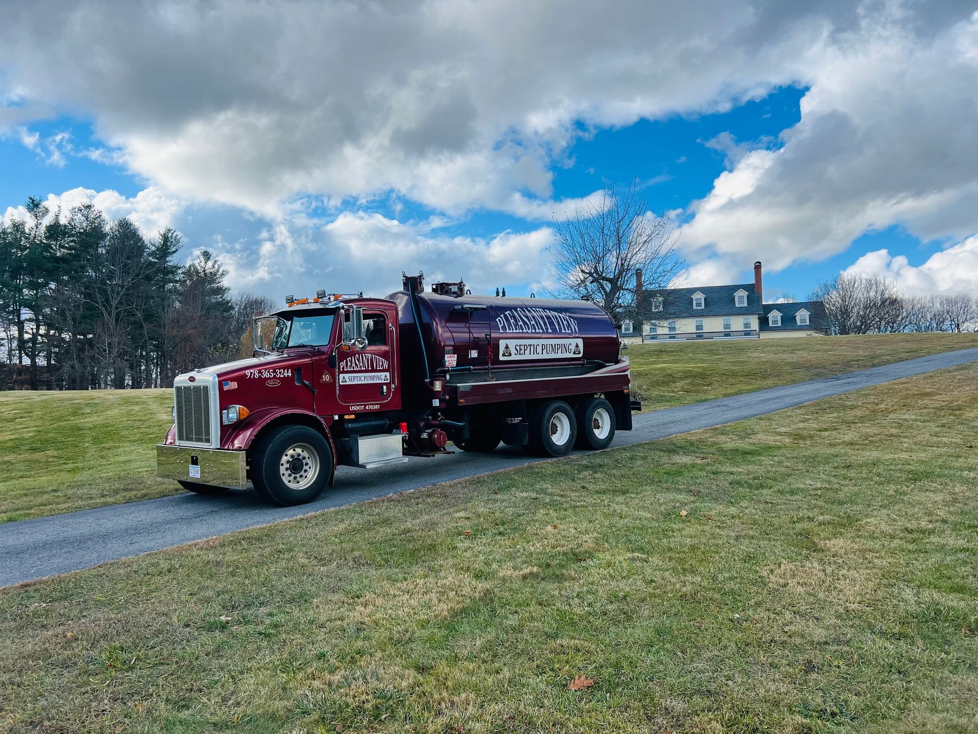 A red truck is parked next to a red portable toilet on a dirt road.