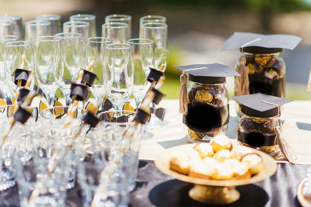 A table with glasses , jars , and graduation caps on it.