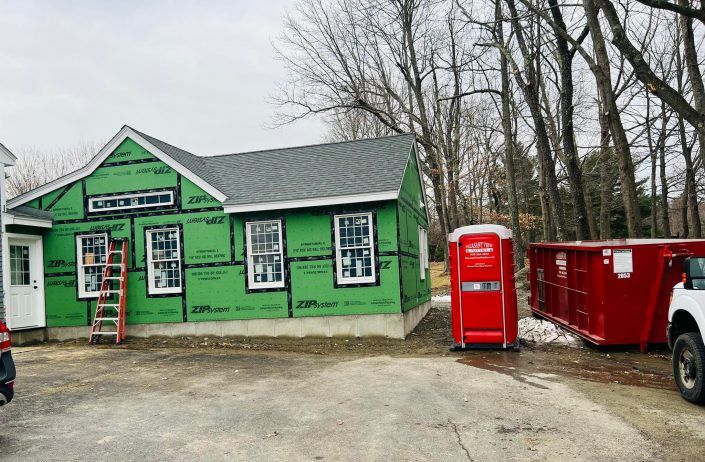 A red dumpster is sitting in front of a house under construction.