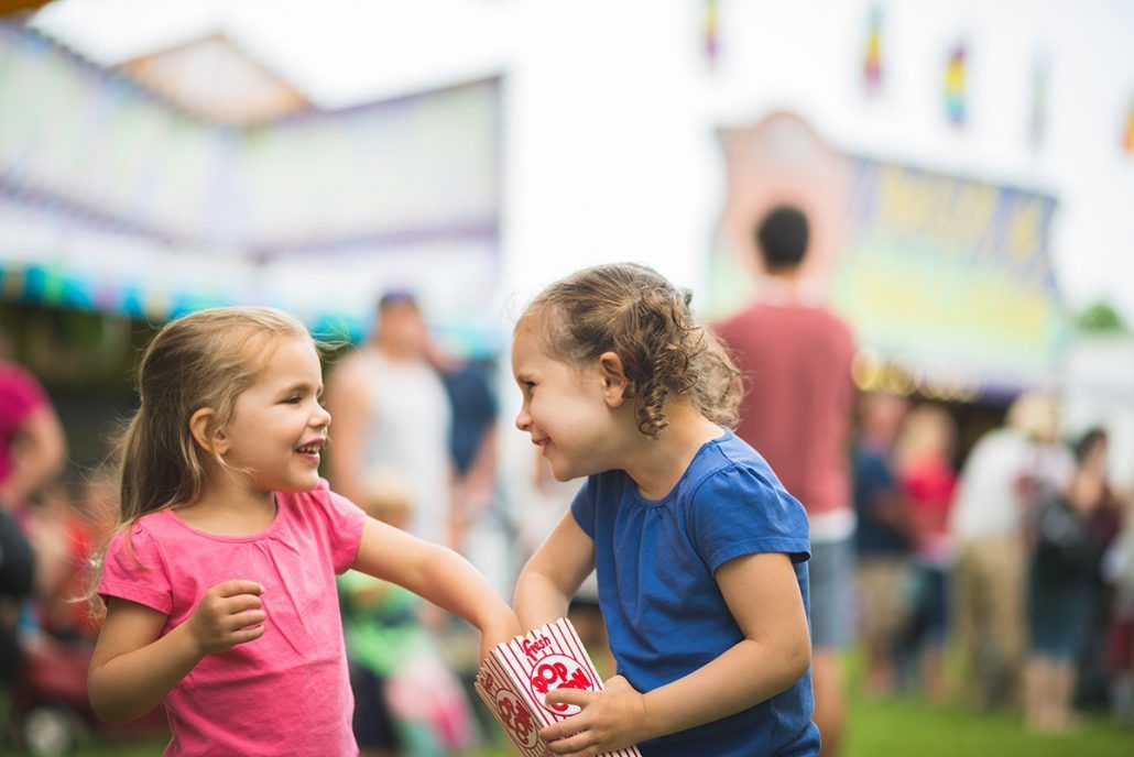 Two little girls are playing with popcorn at a carnival.