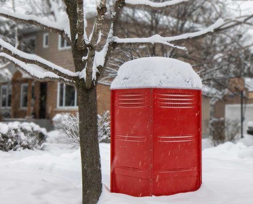 A red trash can is covered in snow in front of a house.