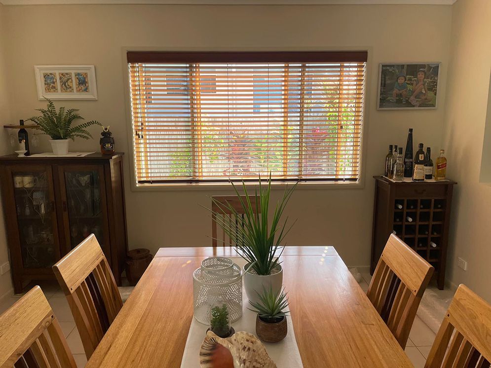 A Dining Room With A Wooden Table And Chairs And A Window With Blinds — Affordable Screens & Blinds in Thabeban, QLD