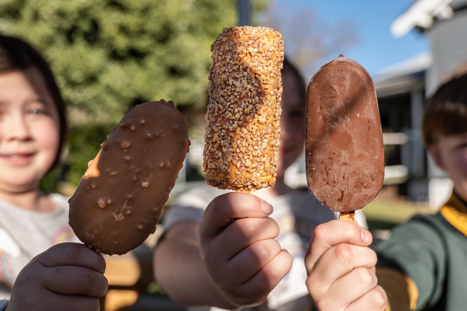 Children holding three different ice cream bars outside.