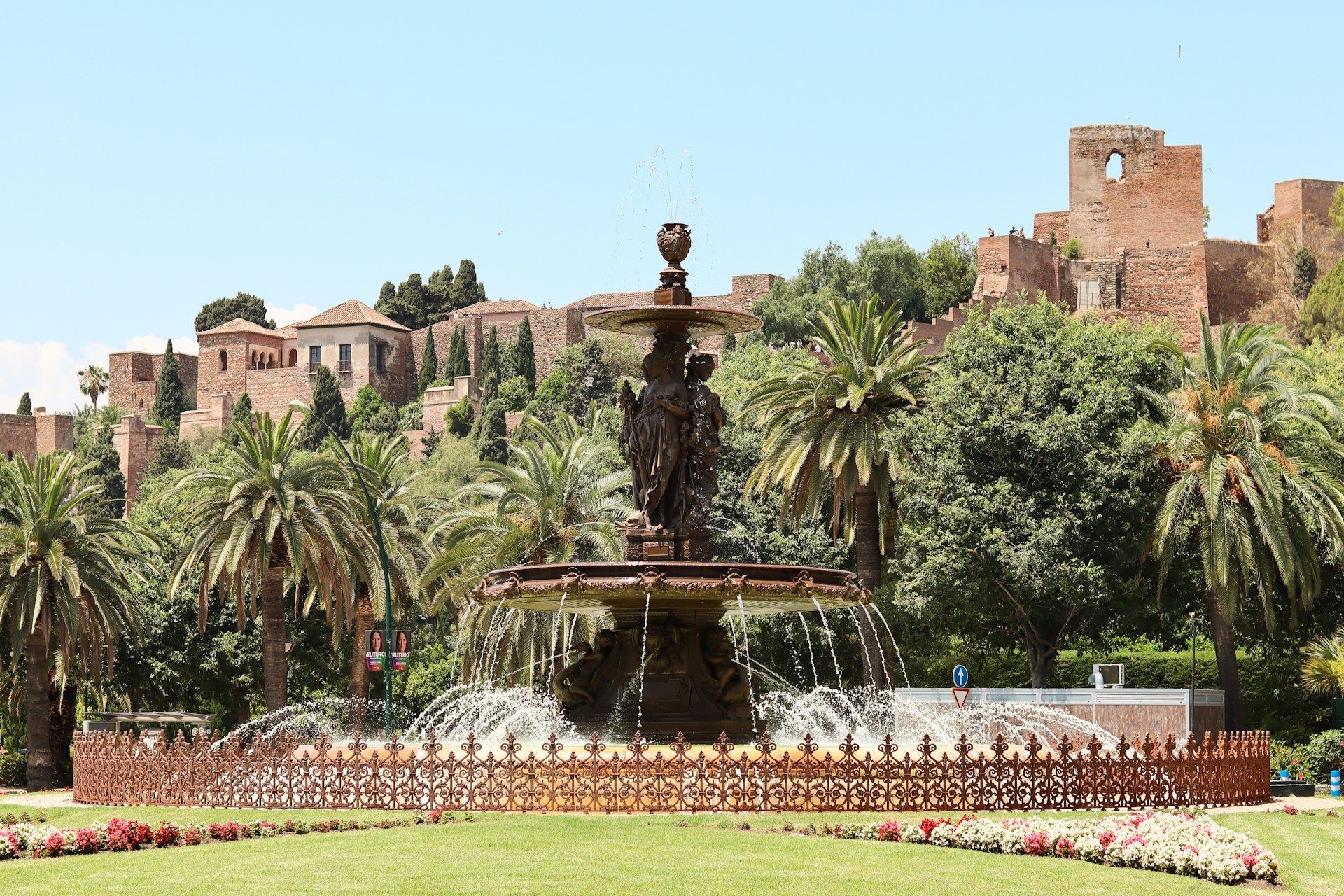 Una fuente en un parque con palmeras y un castillo al fondo.