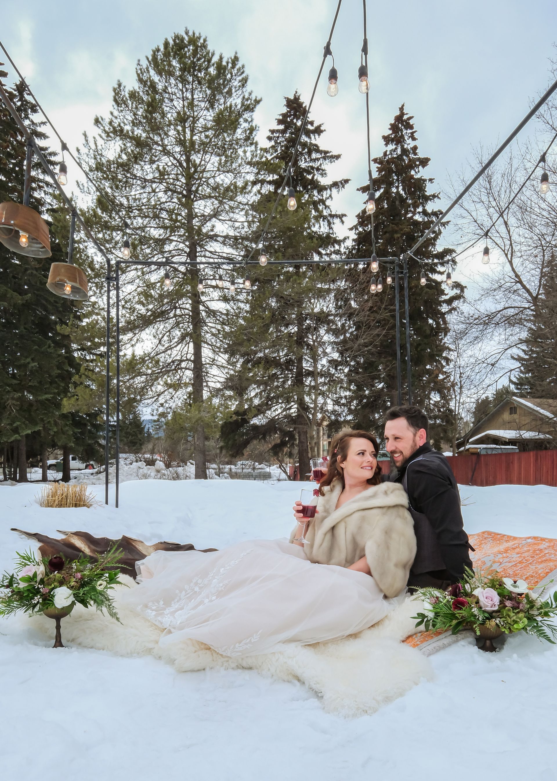 A bride and groom are laying on a blanket in the snow.