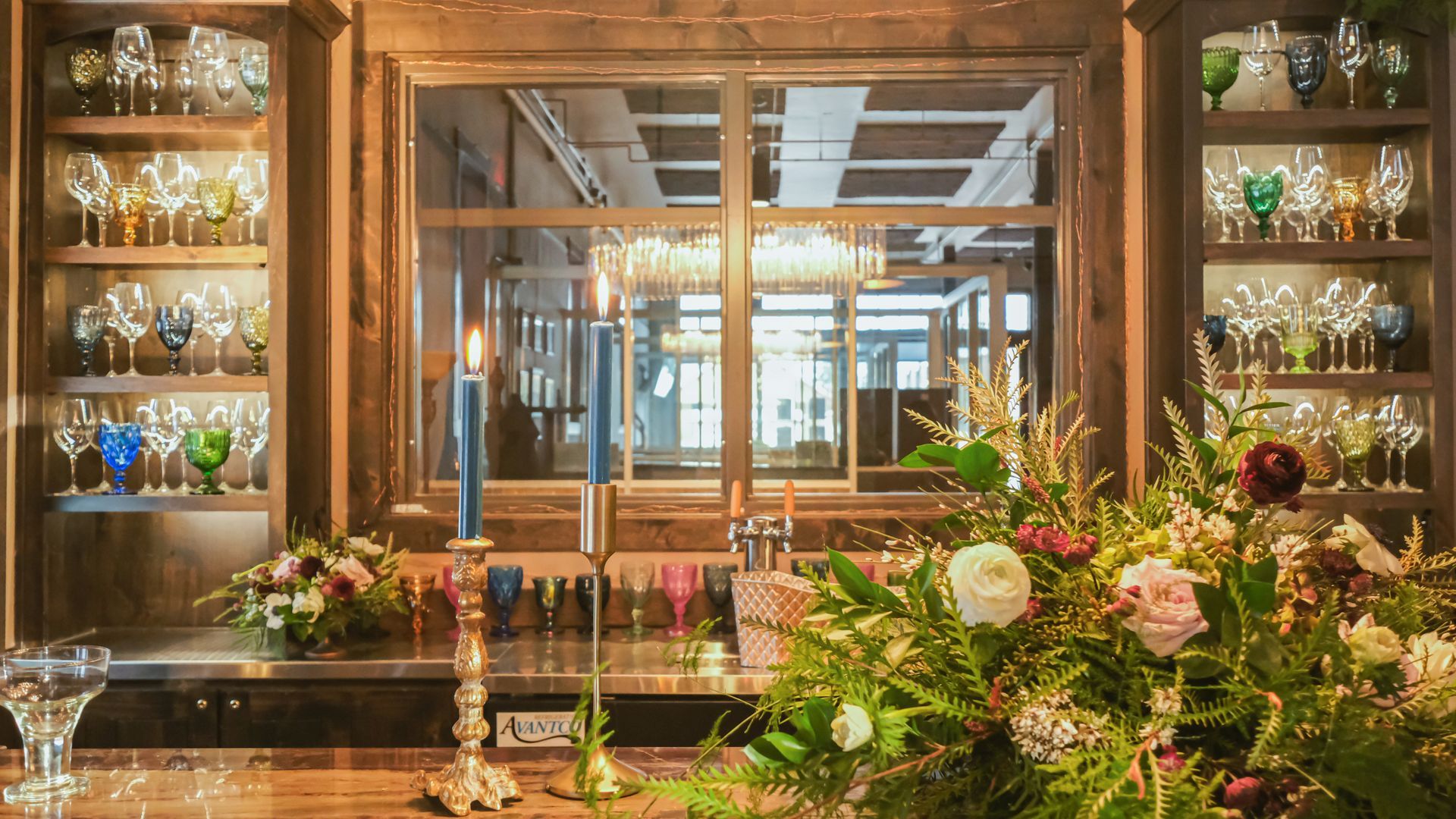 A bar with flowers and candles on it and glasses on the shelves.