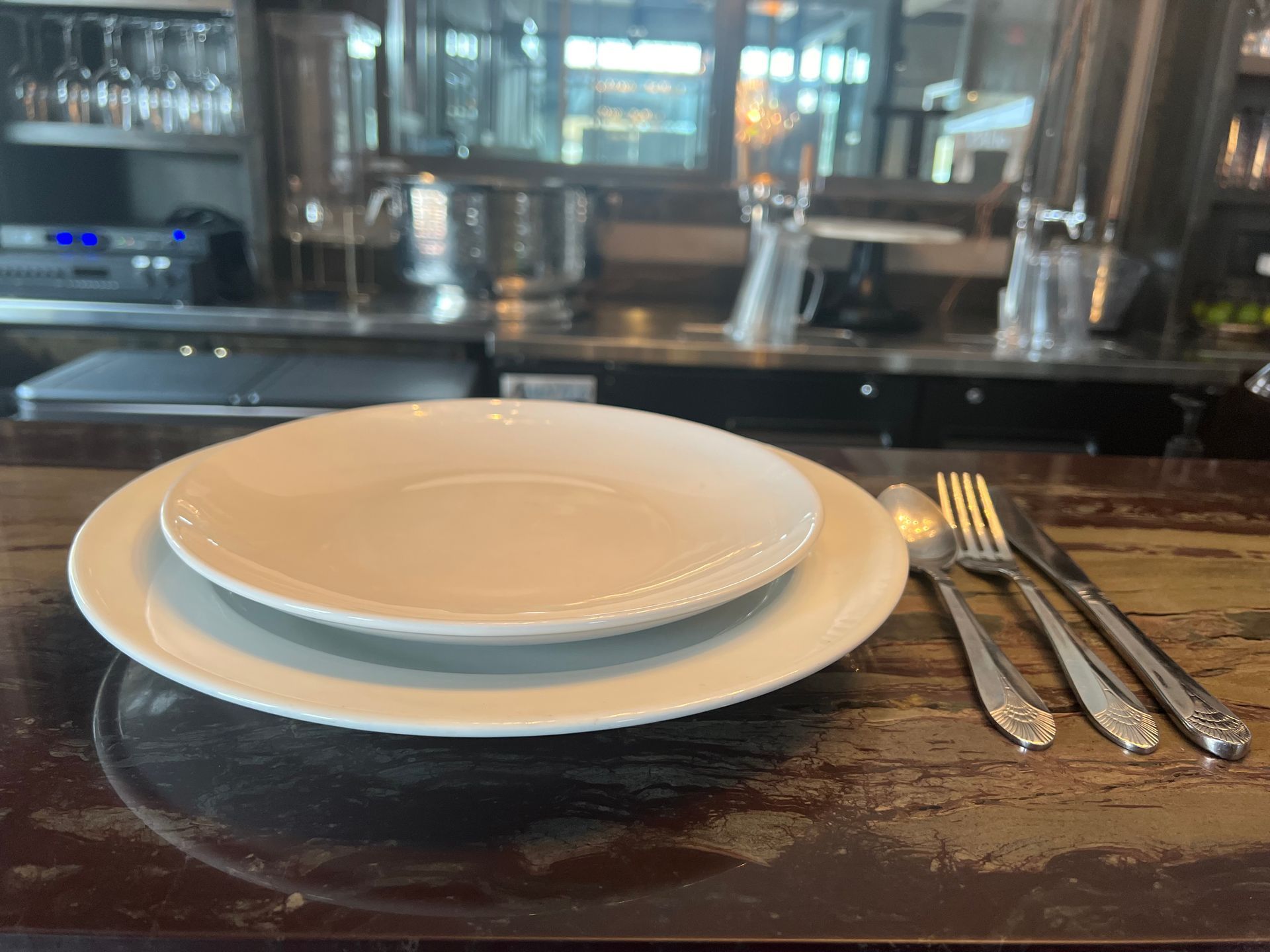 Two white plates and silverware are on a wooden table.