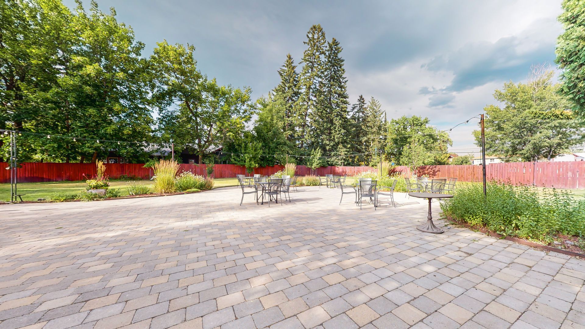 A patio with tables and chairs in a park with trees in the background.