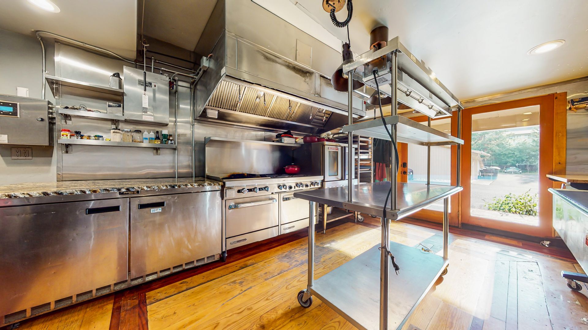 A large kitchen with stainless steel appliances and a wooden floor.
