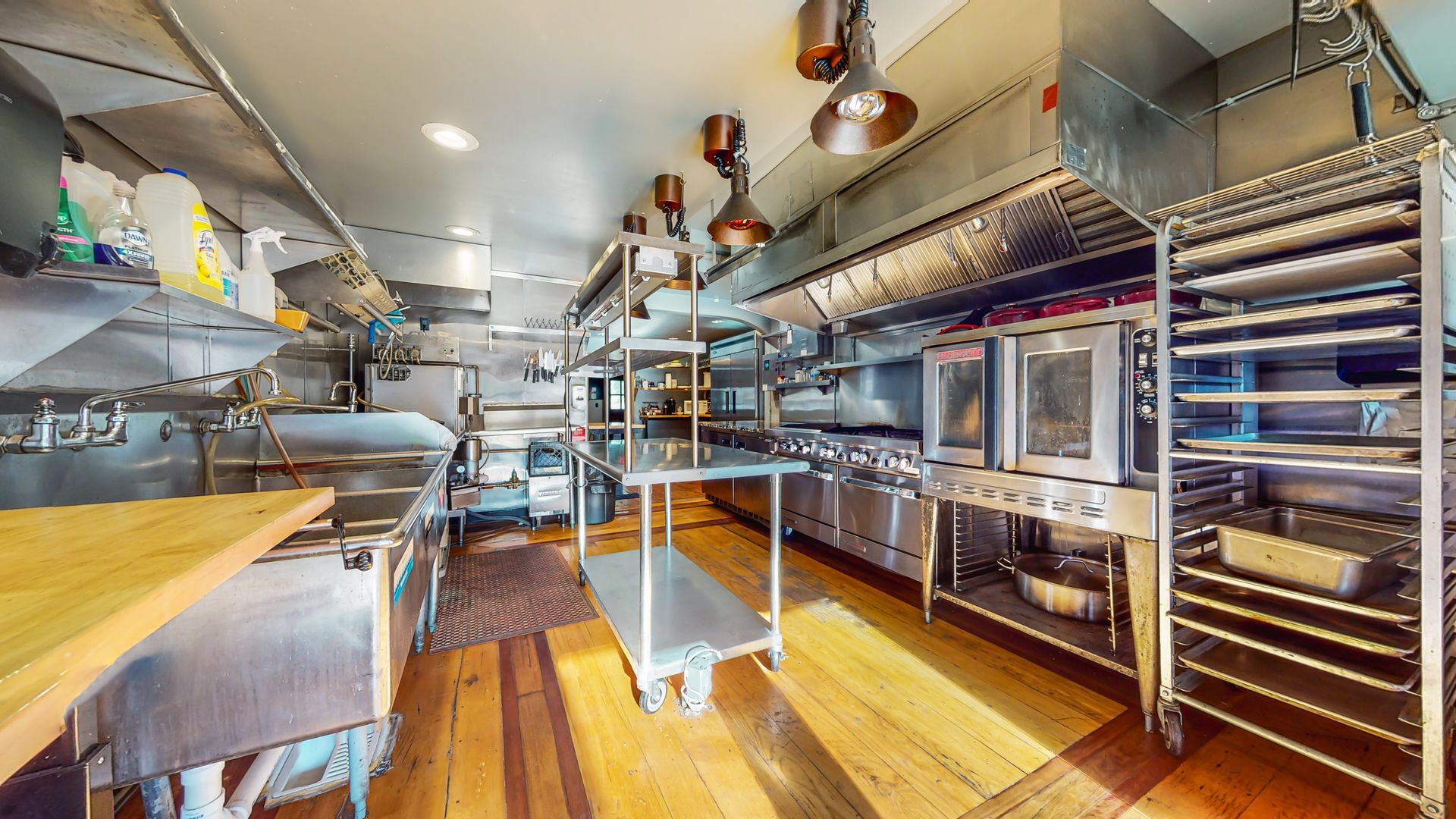 A large kitchen with lots of stainless steel appliances and wooden floors.