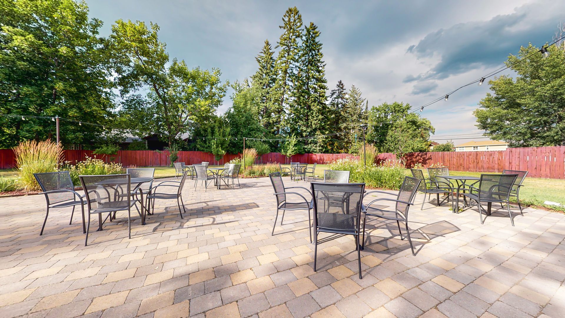 A patio with tables and chairs in a park with trees in the background.