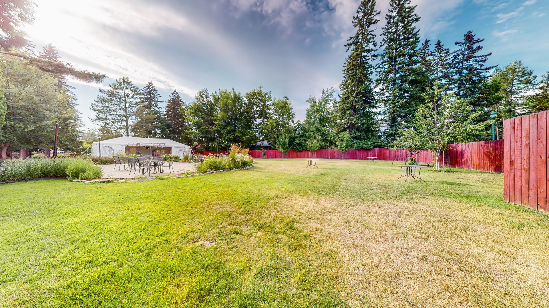 A large lawn with a red fence and trees in the background.