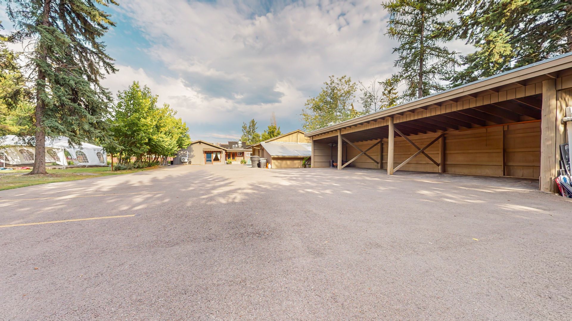 A parking lot with a row of sheds and trees in the background.