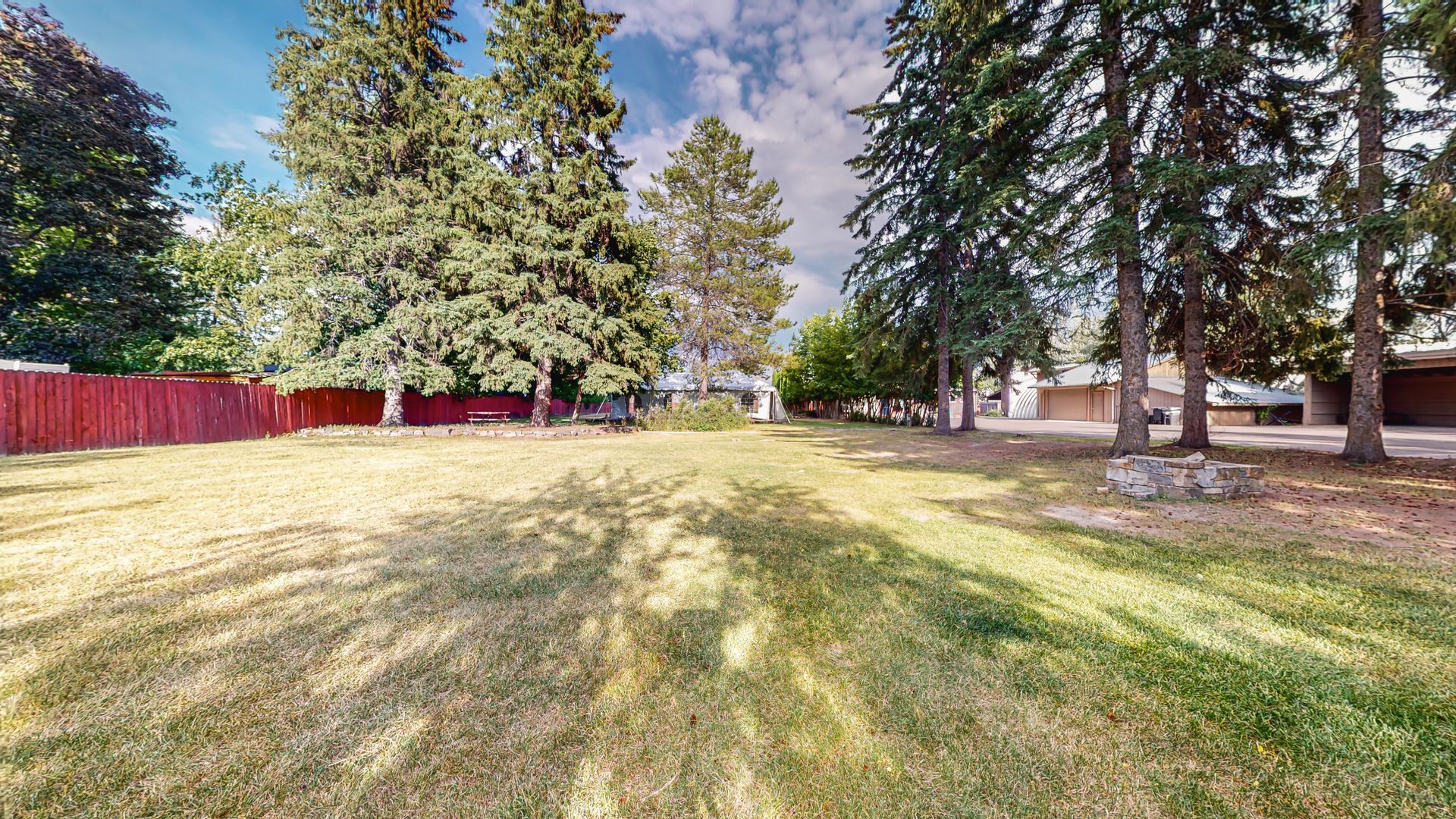 A large grassy field with trees and a red fence in the background.