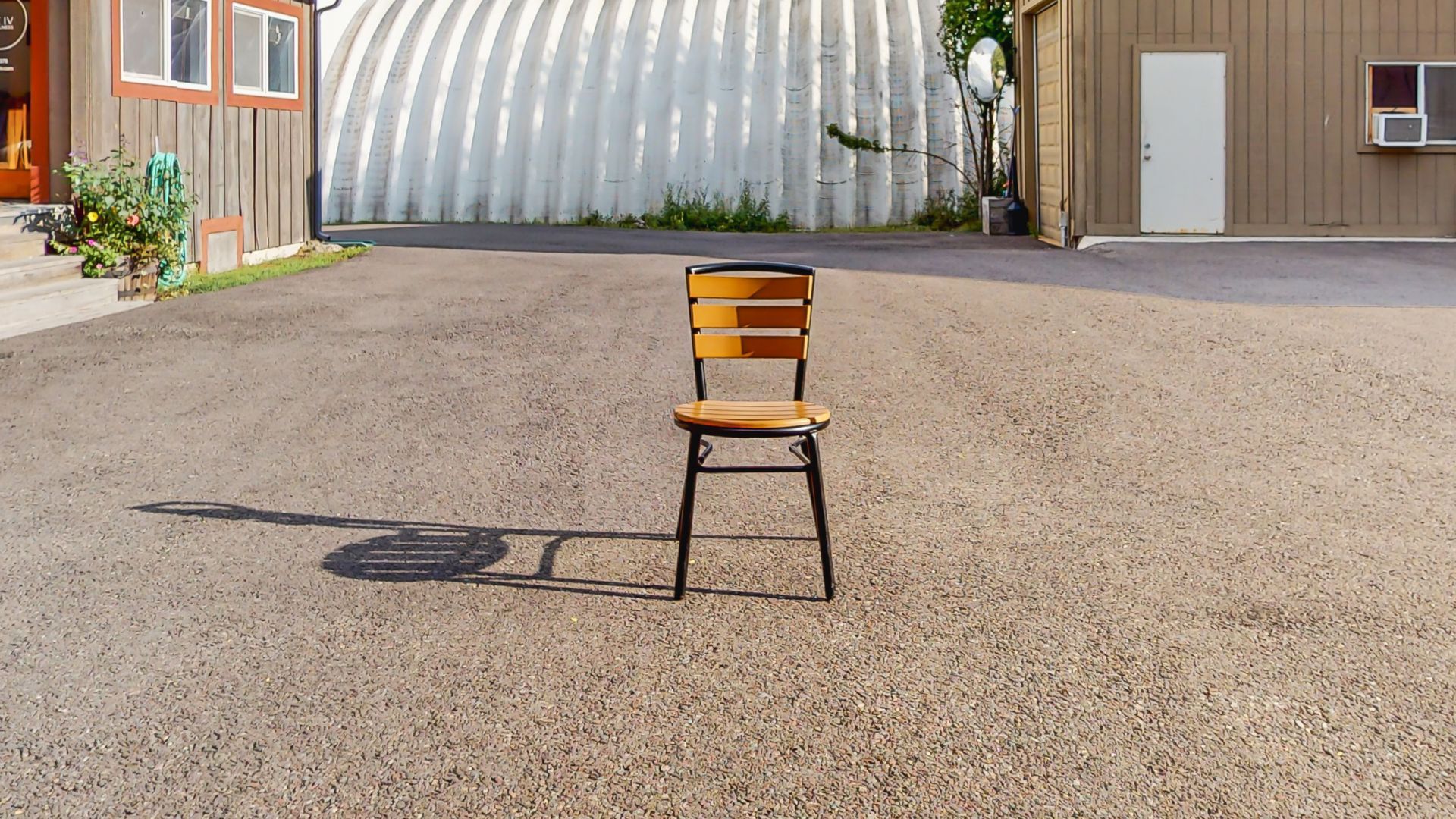 A wooden chair is sitting in the middle of a gravel driveway