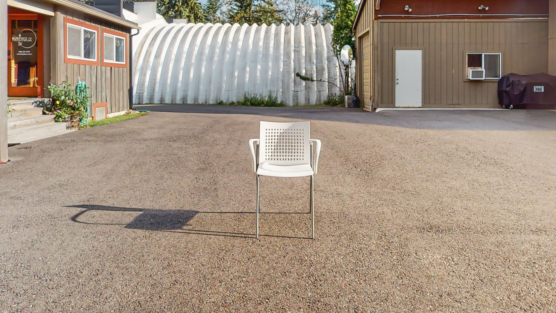 A white chair is sitting in a gravel driveway in front of a house.