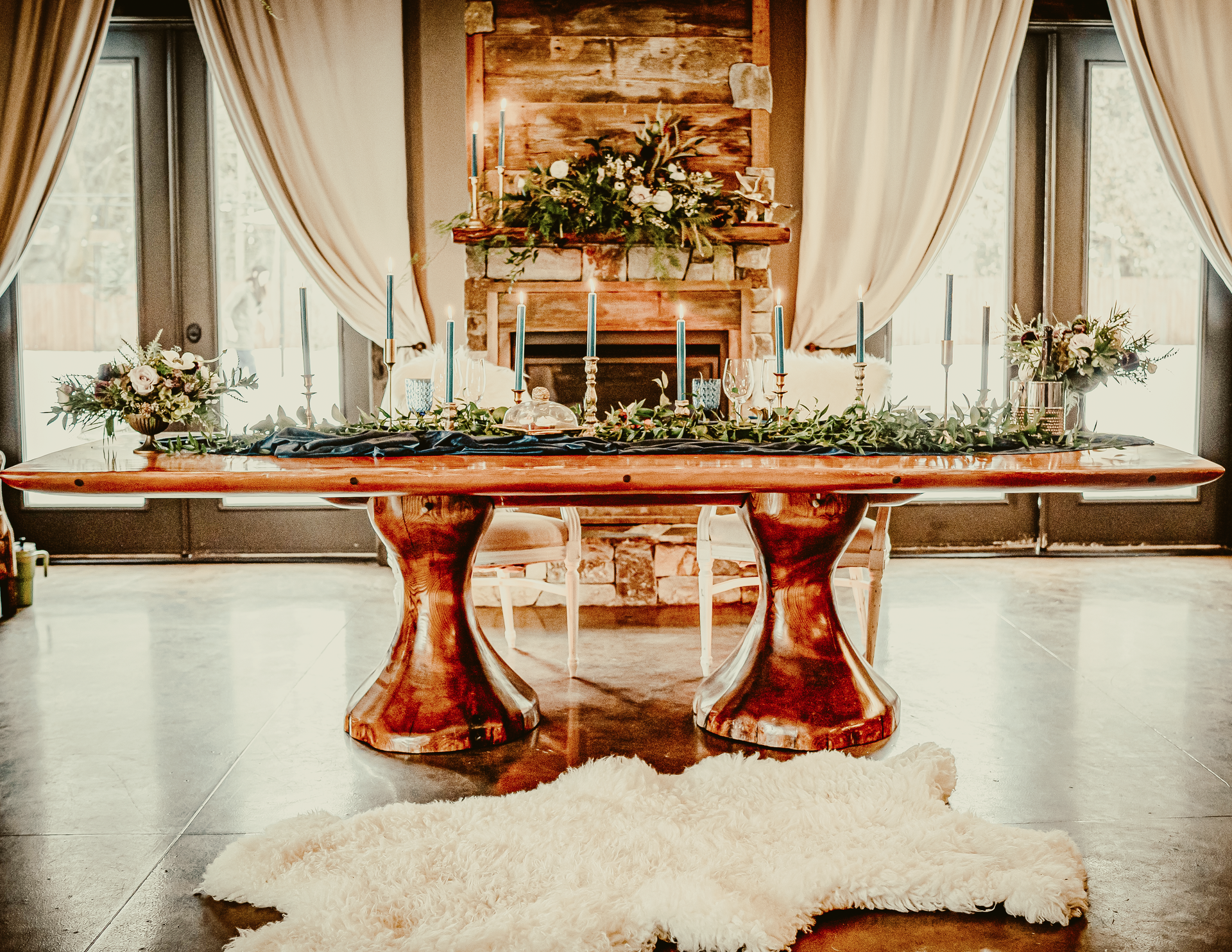 A wooden table with candles and flowers on it in front of a fireplace.