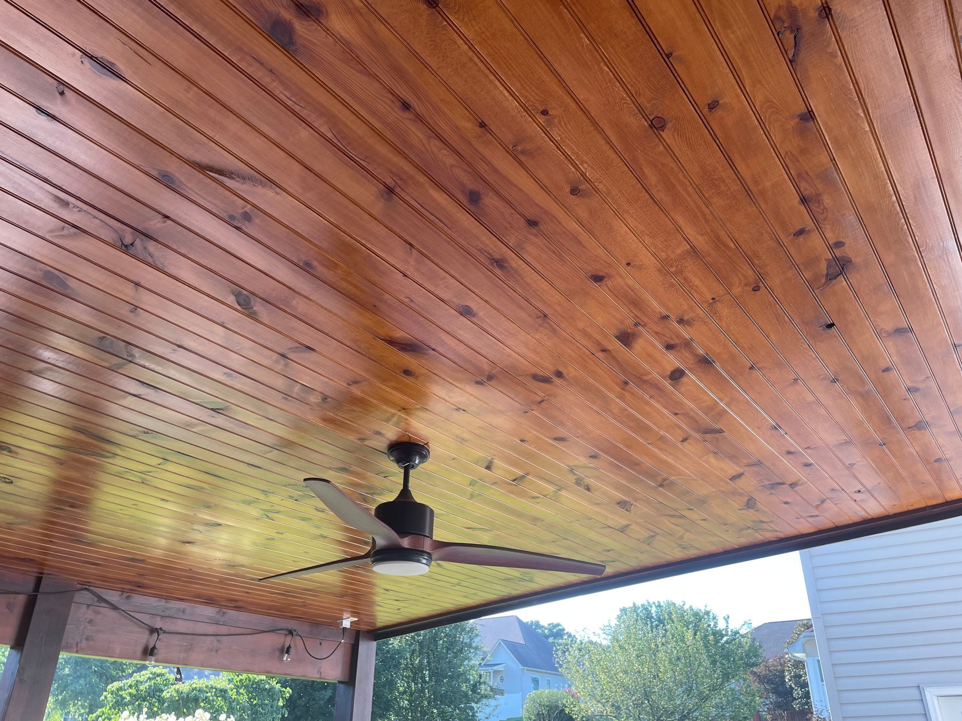 A ceiling fan is hanging from the ceiling of a wooden porch.