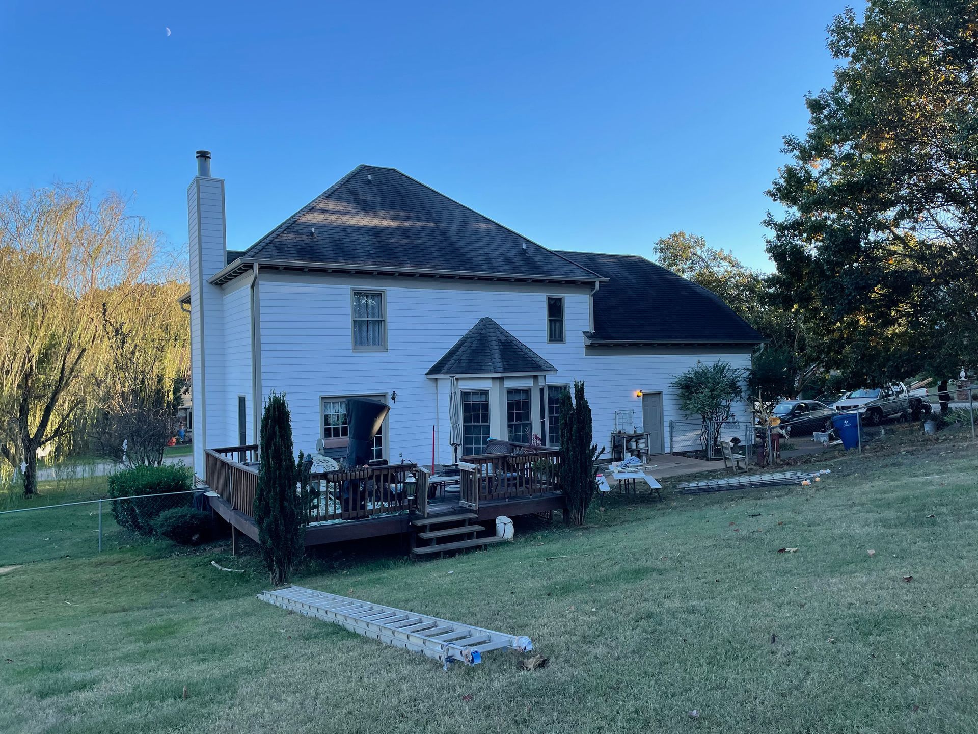 A white house with a black roof and a deck in the backyard.