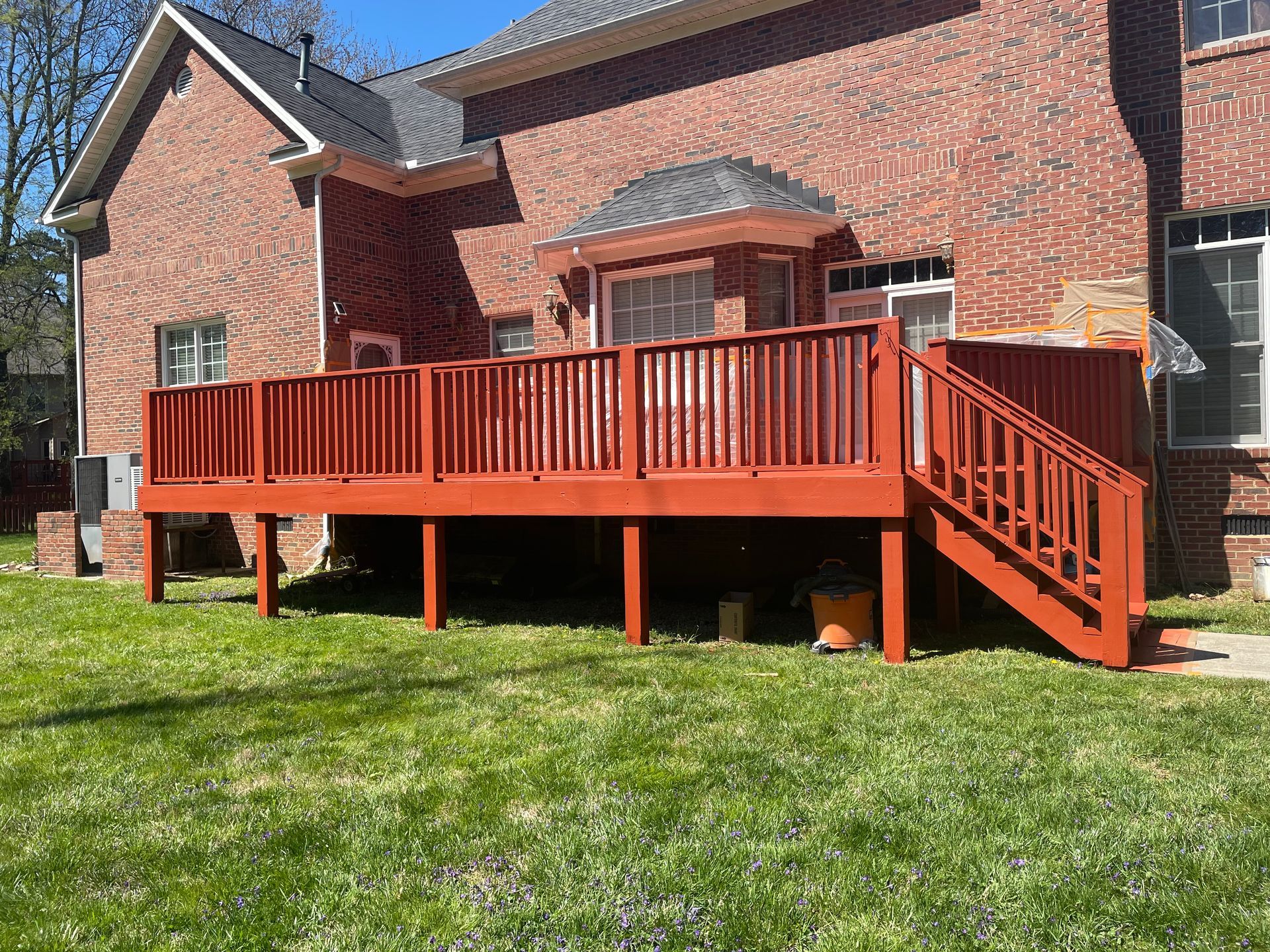 A large wooden deck with stairs is in front of a large brick house.