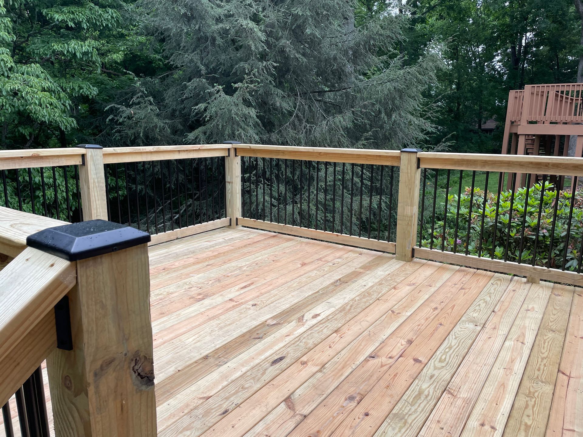 A wooden deck with a metal railing and trees in the background.