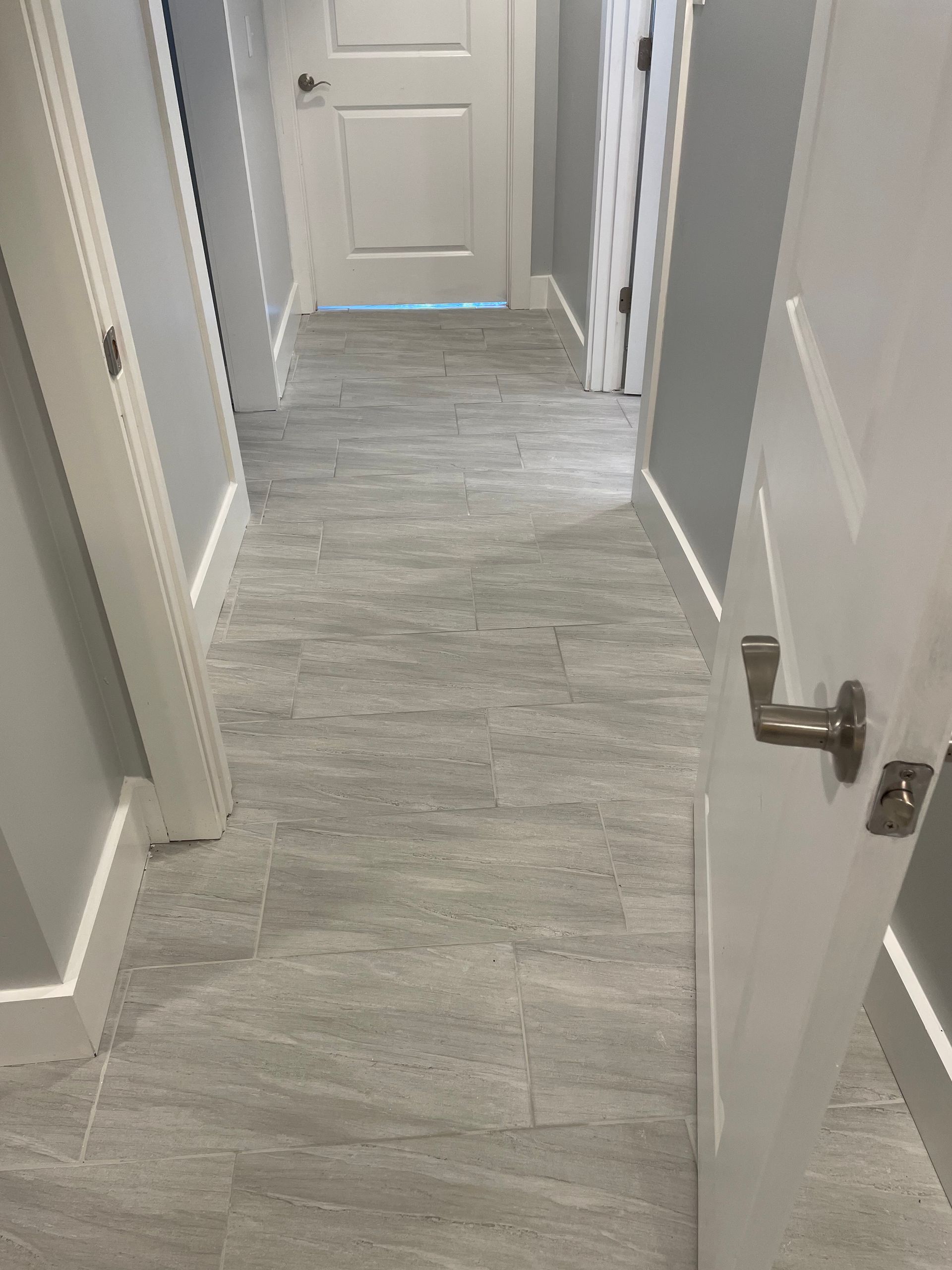A hallway with gray tile floors and white doors.