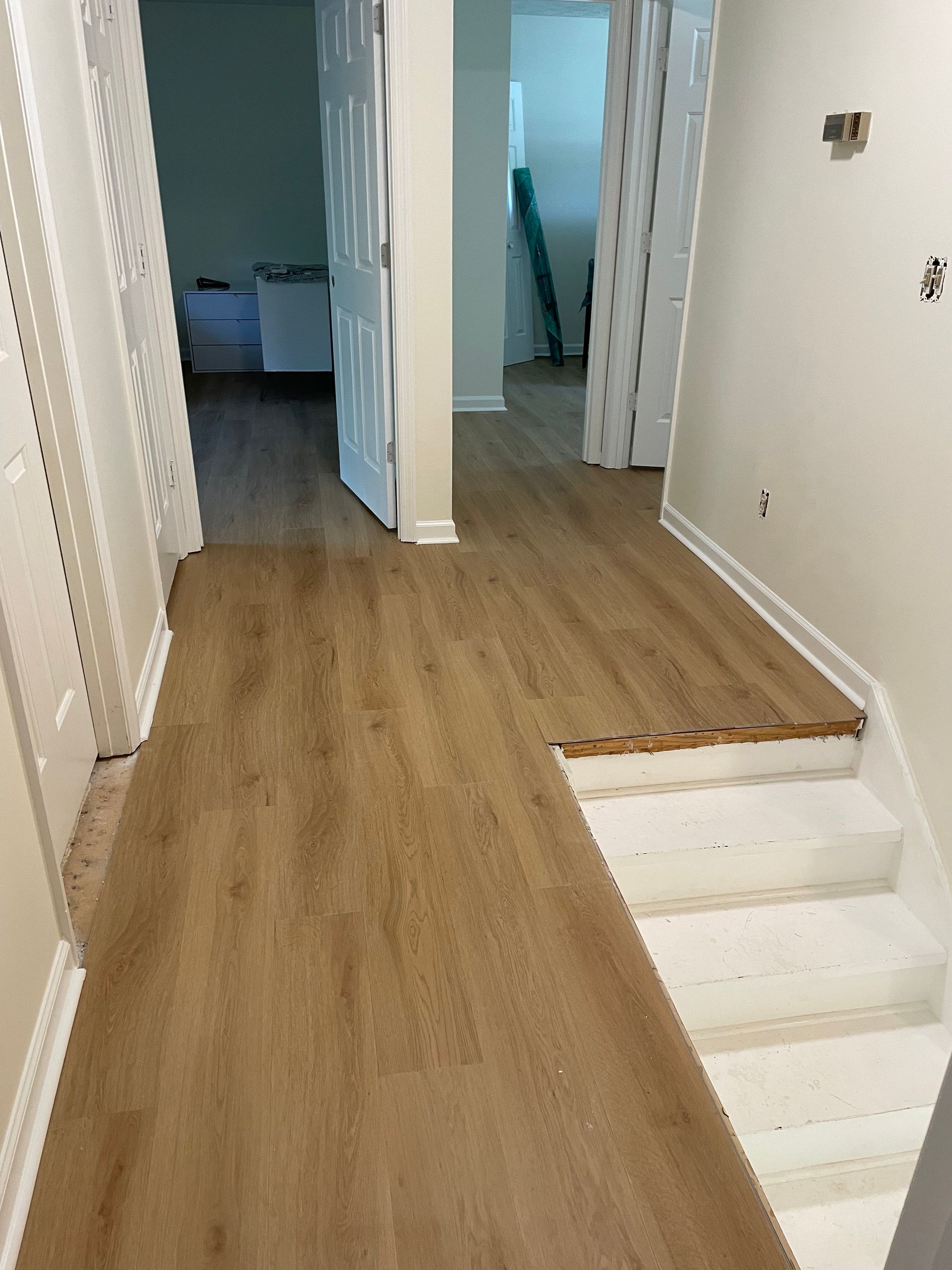 A hallway with hardwood floors and white stairs in a house.