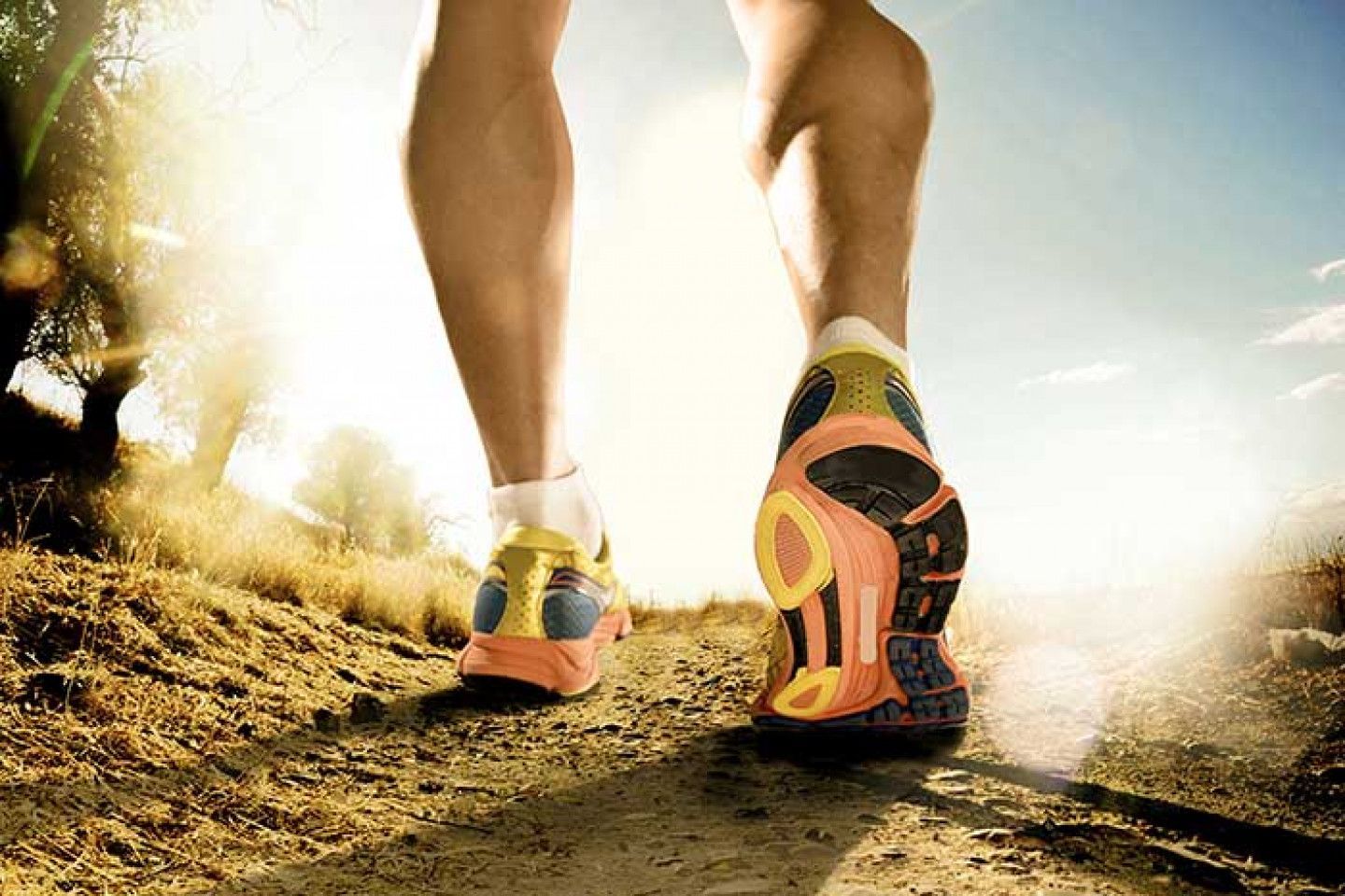 Person's legs in colorful running shoes walking on a dirt path, sunny outdoor setting.