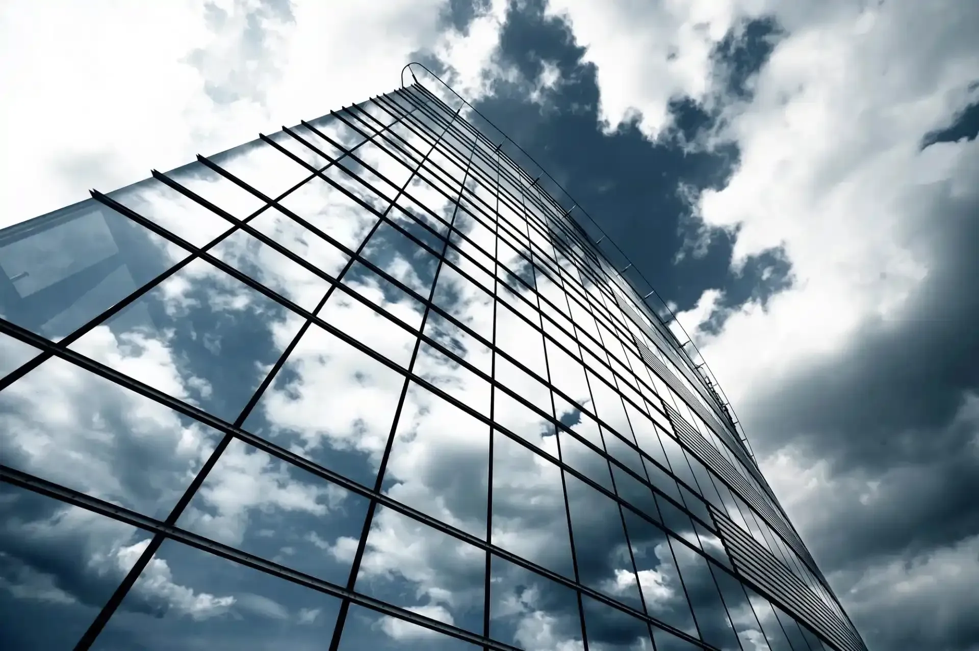 Grattacielo di vetro che riflette il cielo nuvoloso, visto da un'angolazione bassa.