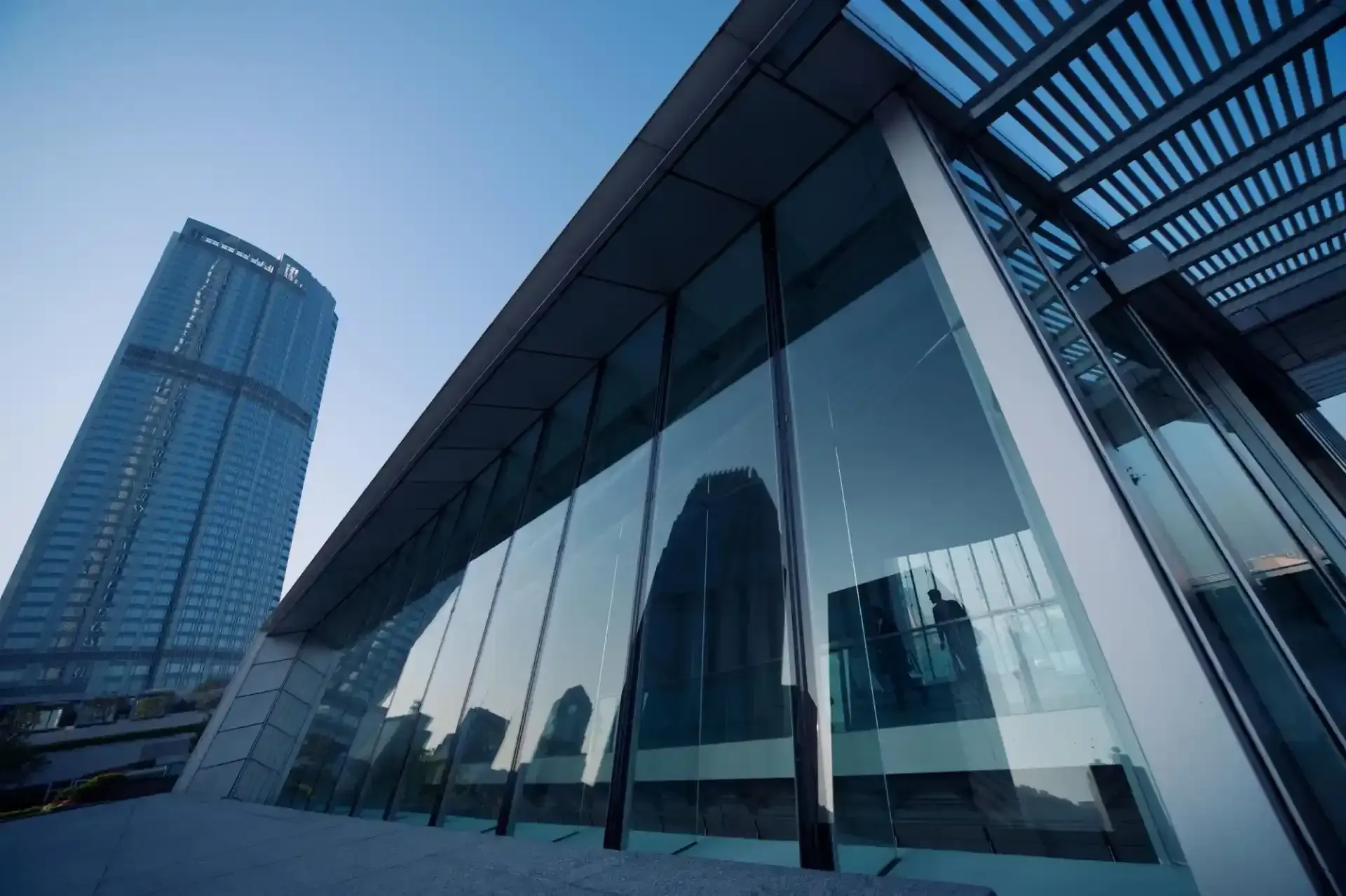 Moderno edificio in vetro con un grattacielo sullo sfondo, contro un cielo blu.