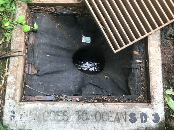 Open storm drain with a black fabric insert and an embossed message: