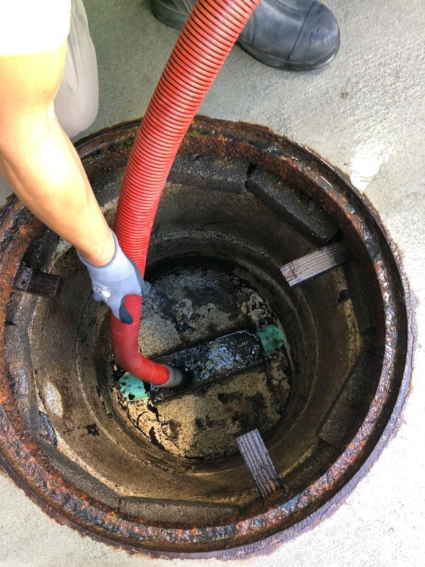 A person in a protective glove uses a red suction hose to clean the bottom of an open, circular industrial utility vault.