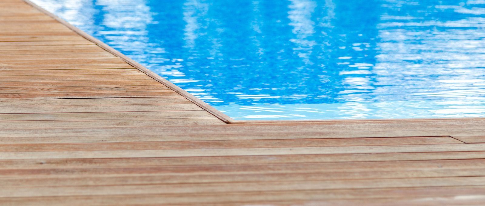 Wooden deck edging a swimming pool with blue water.