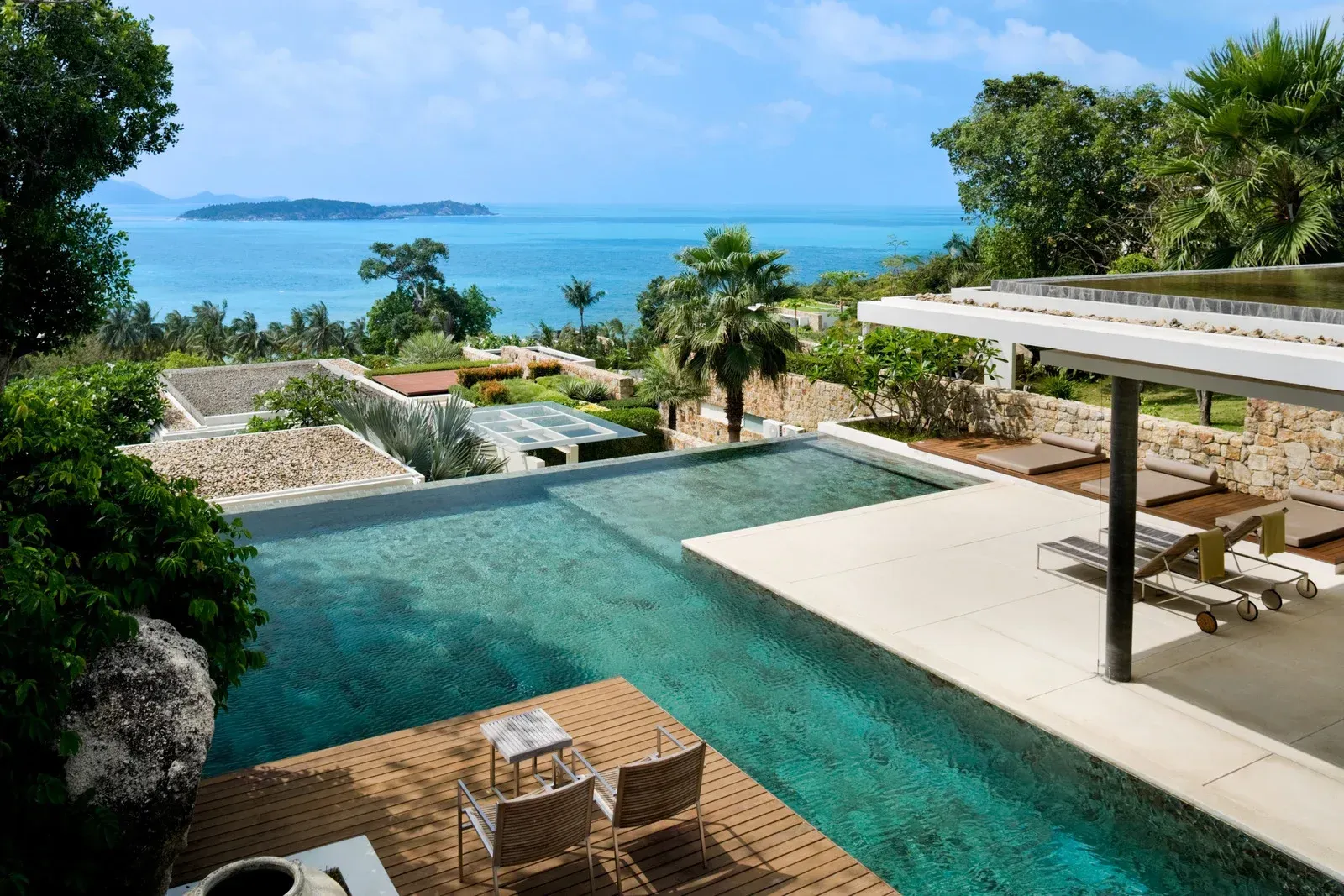 Infinity pool overlooking ocean, lounge chairs, tropical foliage.