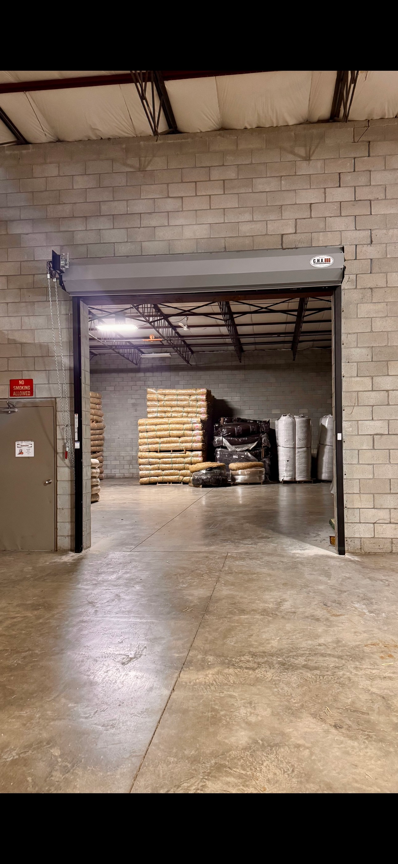 A warehouse with a roller door open and pallets on the floor.