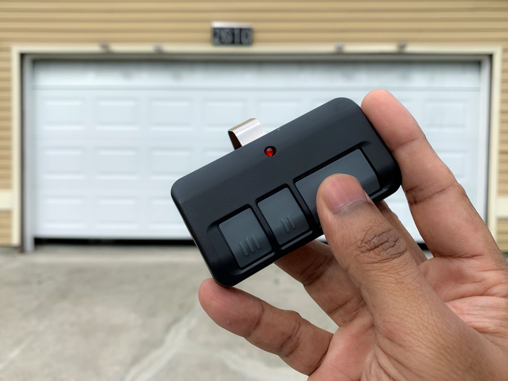 A person is holding a remote control in front of a garage door.