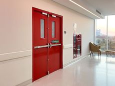 A hospital hallway with red doors and a fire extinguisher.